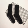 A pair of black mid-calf yoga and pilates socks laid on a black grid mat.