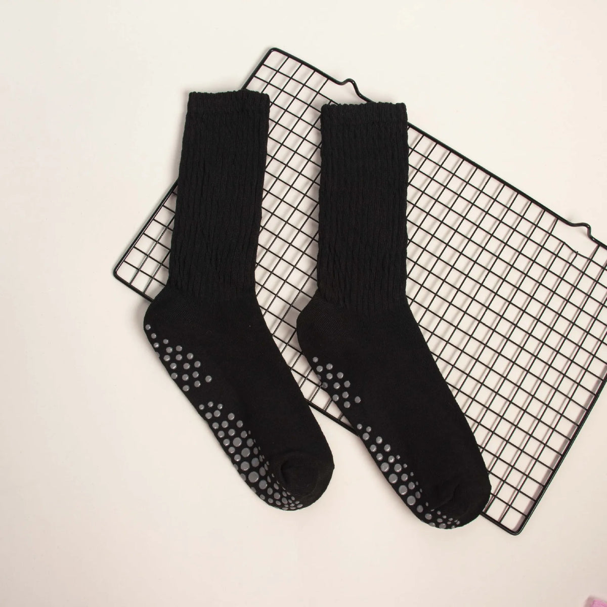 A pair of black mid-calf yoga and pilates socks laid on a black grid mat.