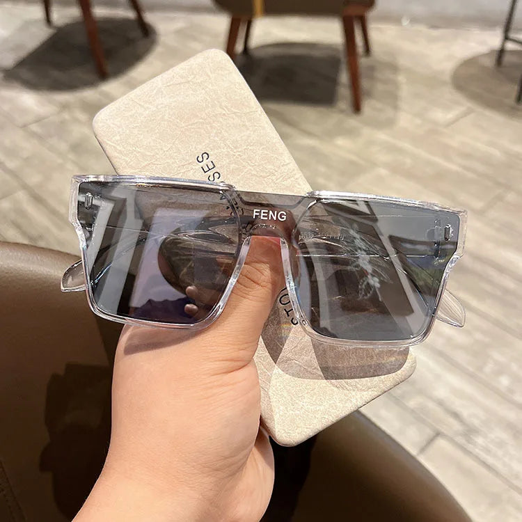 A hand holds a pair of clear acetate sunglasses resting on a light beige card.