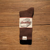 A brown tube sock with a white quality label is displayed on a wooden surface.