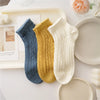 Three pairs of breathable mesh lace tube socks in blue, yellow, and cream stacked on a white tray.