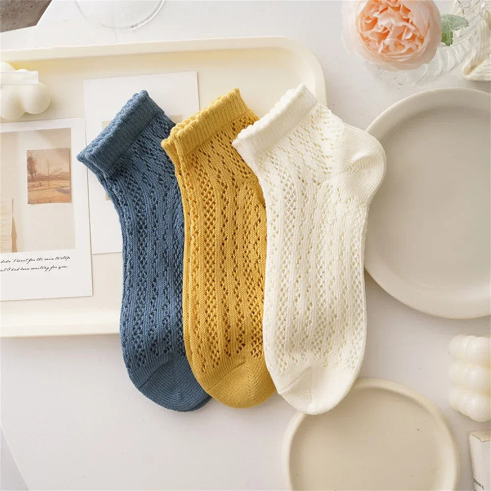 Three pairs of breathable mesh lace tube socks in blue, yellow, and cream stacked on a white tray.