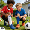 Dos niños con uniformes de fútbol azules y rojos arrodillados en un campo de hierba con balones cerca.