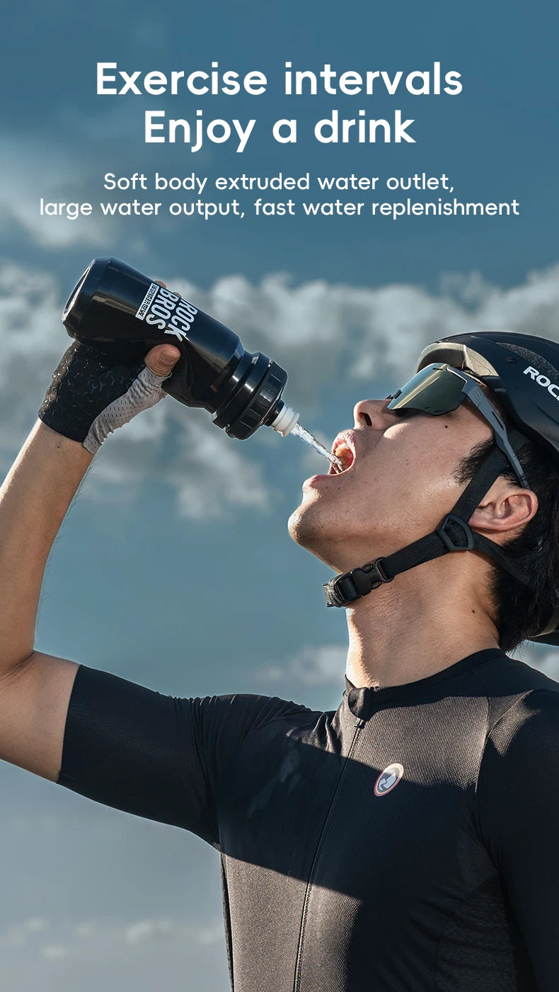 A man is drinking from a black sports water bottle outdoors, enjoying hydration during exercise.