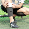 A person is wearing black soccer shin guards and a white knee brace while practicing on a grassy field.