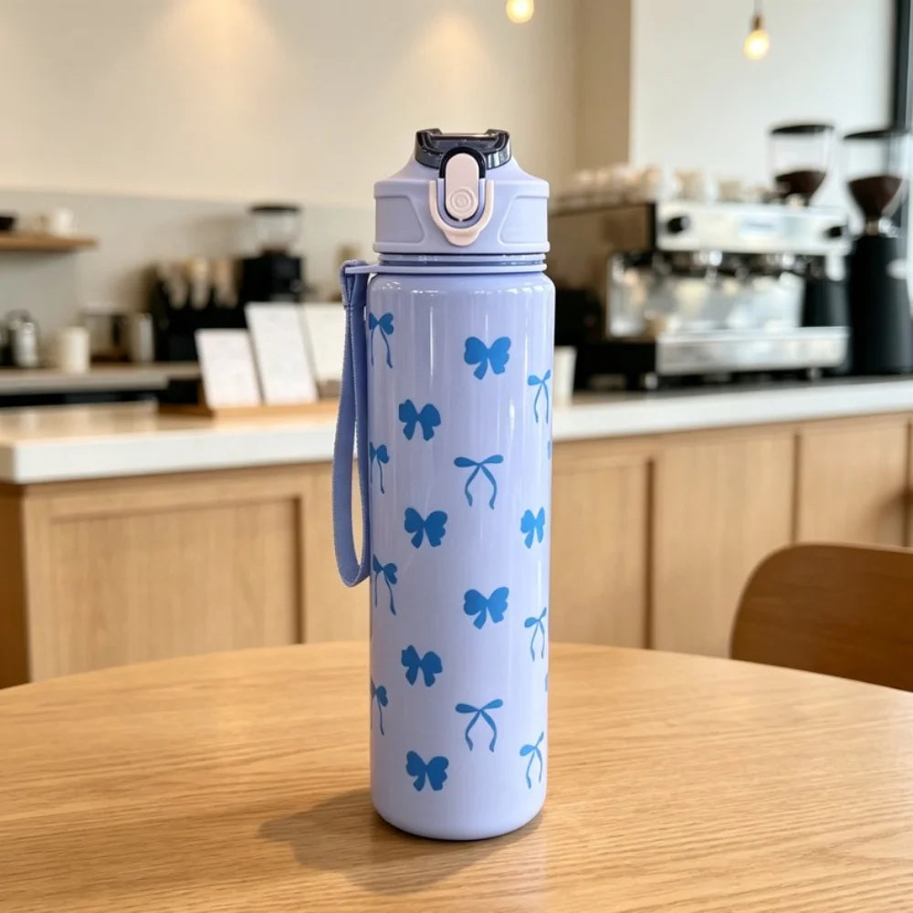 A light blue reusable water bottle with a pink lid and a pattern of blue butterfly decals sitting on a wooden table.