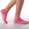 Pink yoga socks with rainbow trim worn on a person's foot and ankle.
