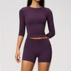 A woman wearing a purple long-sleeved top and matching high-waisted leggings set for yoga and fitness.
