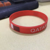 A red silicone wristband with the flag of Qatar printed on it, resting on a light surface.