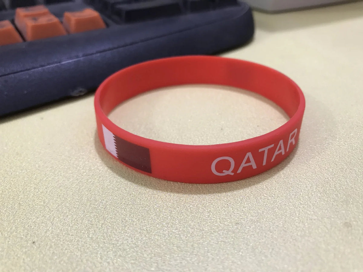 A red silicone wristband with the flag of Qatar printed on it, resting on a light surface.