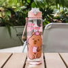 A pink cartoon drinking water bottle with a bear design and straw, sitting on a wooden surface.