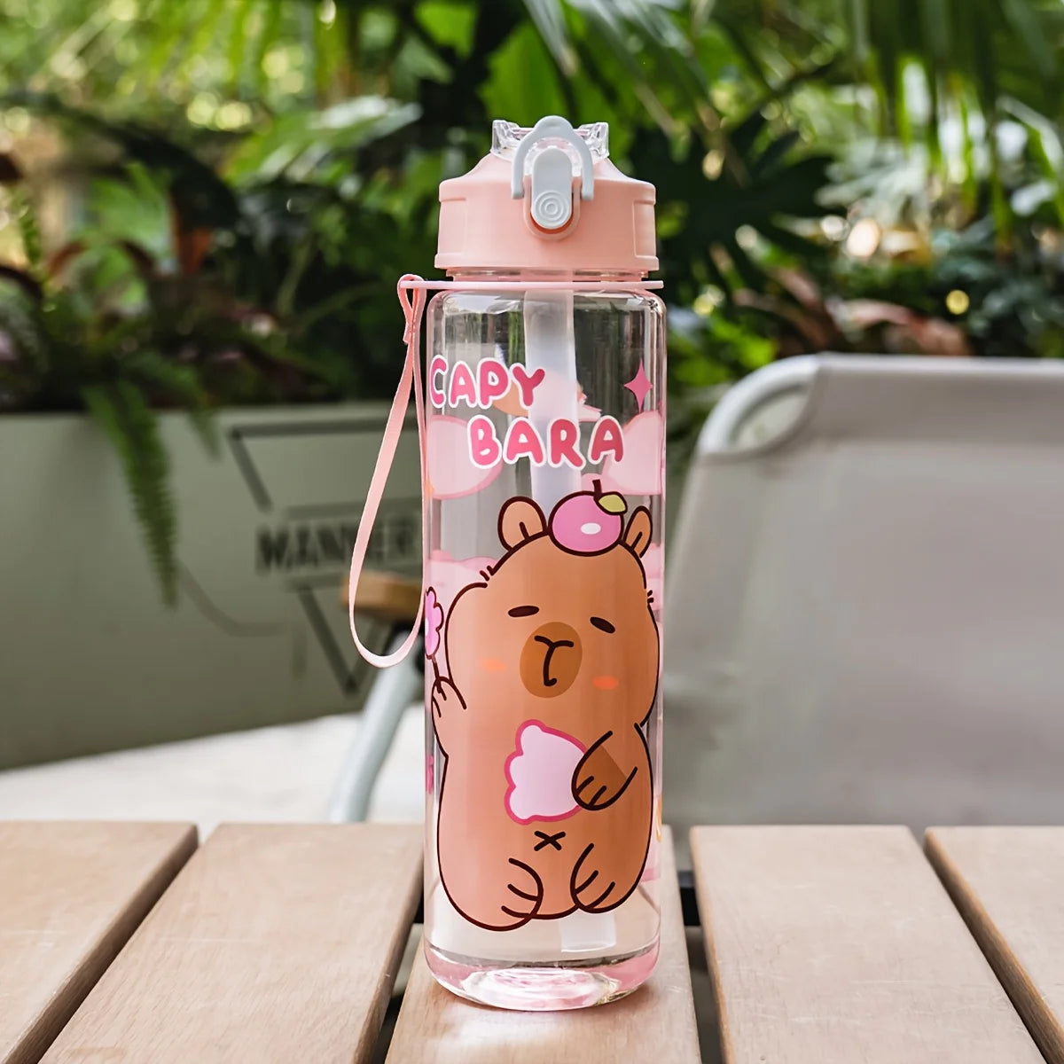 A pink cartoon drinking water bottle with a bear design and straw, sitting on a wooden surface.