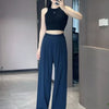 A woman models dark blue loose sports yoga pants and a black crop top in a modern indoor setting.