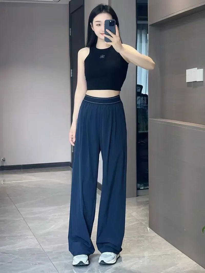 A woman models dark blue loose sports yoga pants and a black crop top in a modern indoor setting.