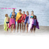 A group of seven models wearing colorful, draped fabric and swimwear posing outdoors near water.