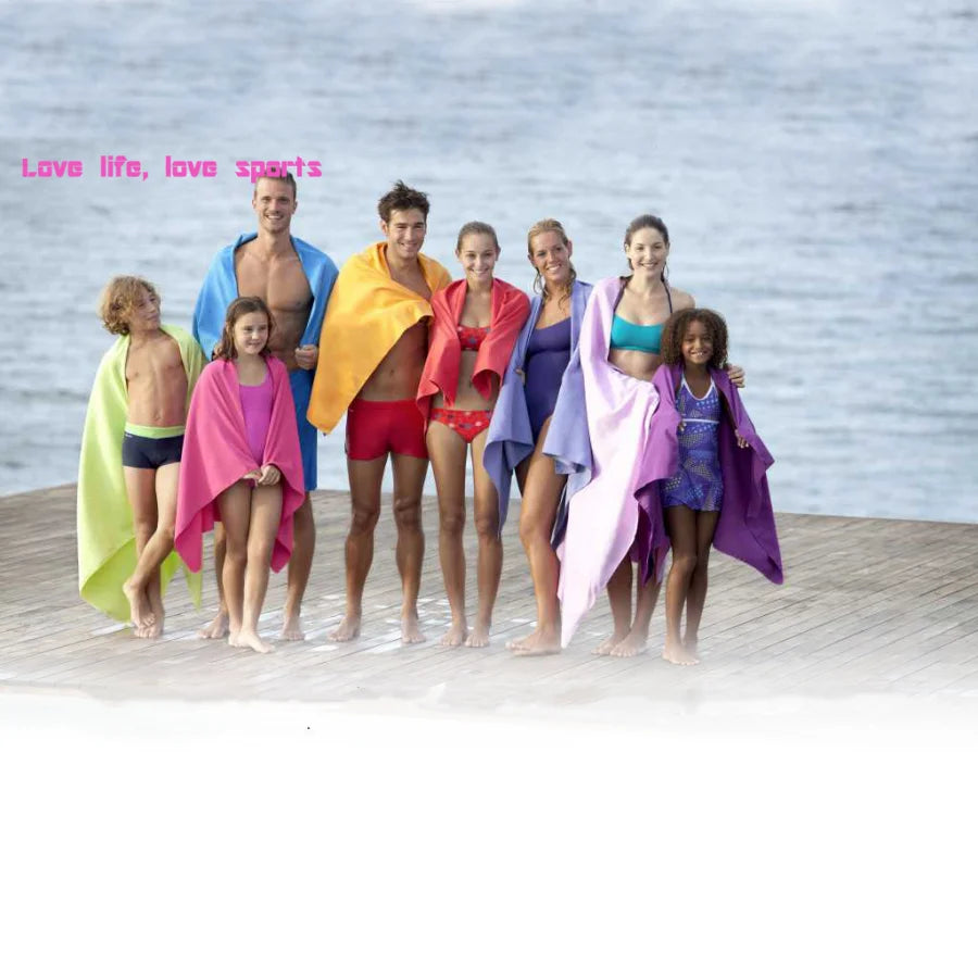 A group of seven models wearing colorful, draped fabric and swimwear posing outdoors near water.