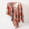A flowing women's silk paisley shawl scarf in shades of rust, blue, and cream draped on a white surface.