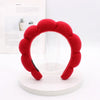 A bright red sponge terry cloth headband for hair styling displayed on a white circular stand.