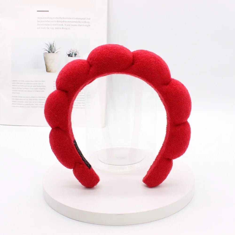 A bright red sponge terry cloth headband for hair styling displayed on a white circular stand.