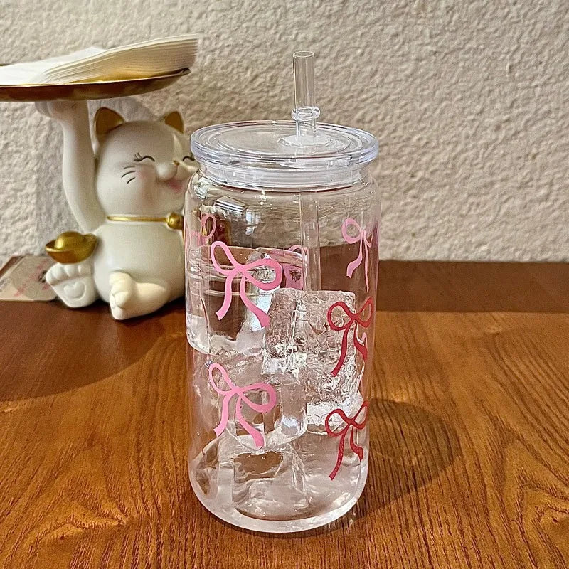 A clear glass tumbler filled with ice and pink ribbon decorations sits next to a white cat figurine.