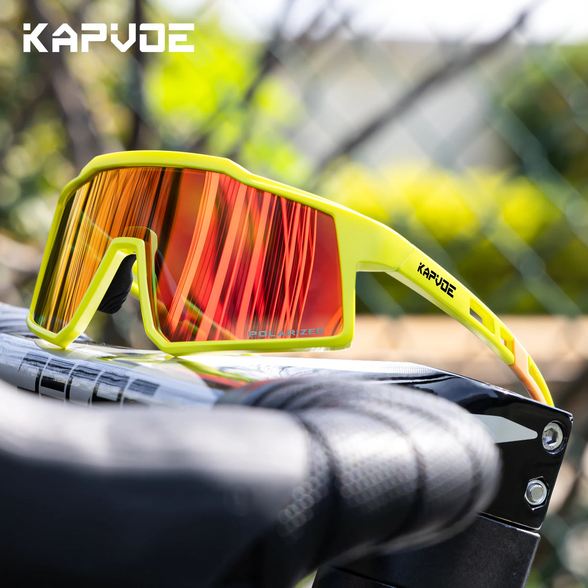A pair of bright yellow polarized sports sunglasses with orange-red lenses resting on a bicycle handlebar.