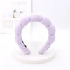 A lavender sponge terry cloth headband for hair styling displayed on a white circular stand.