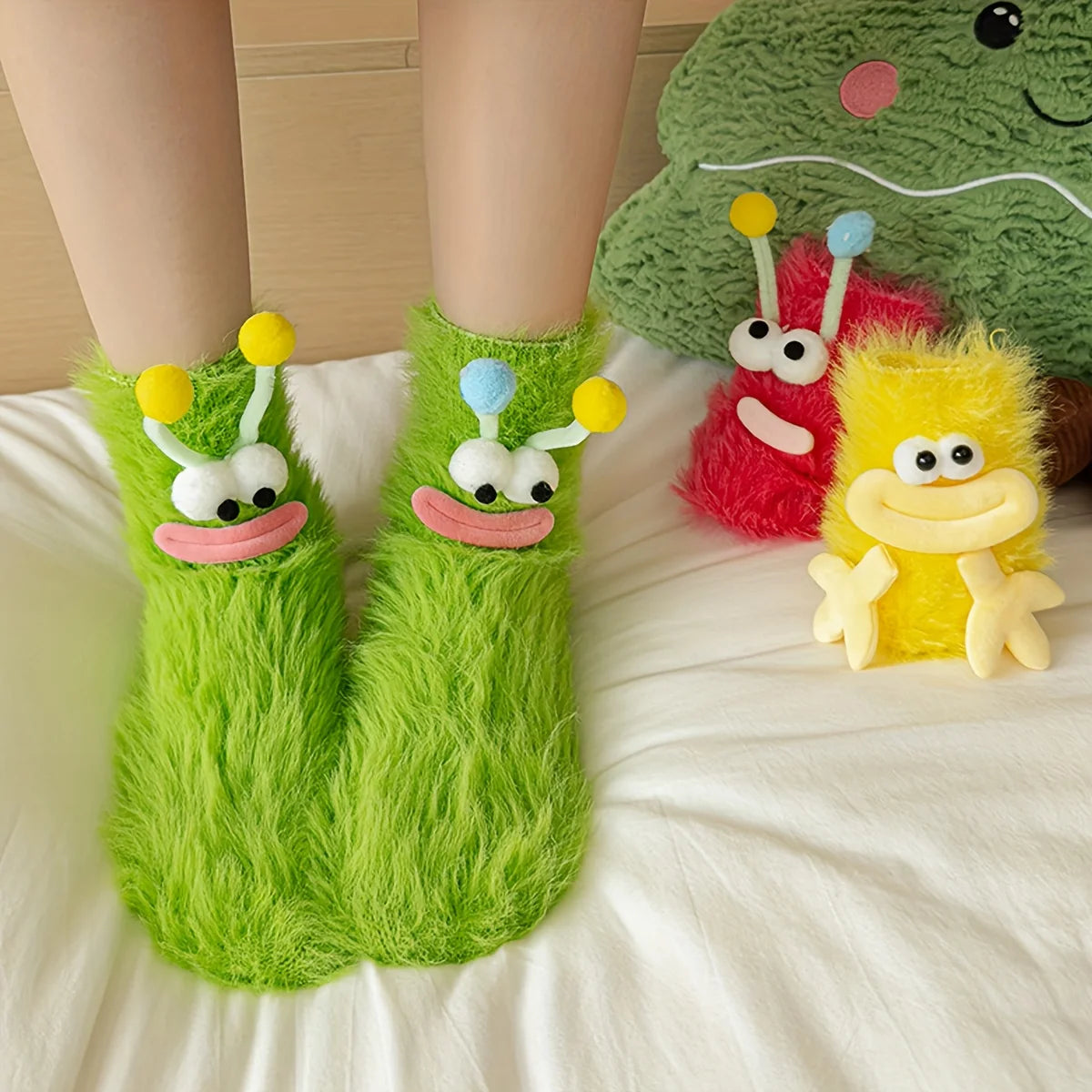 A pair of green plush caterpillar floor socks next to a green dinosaur toy and a yellow plush creature.
