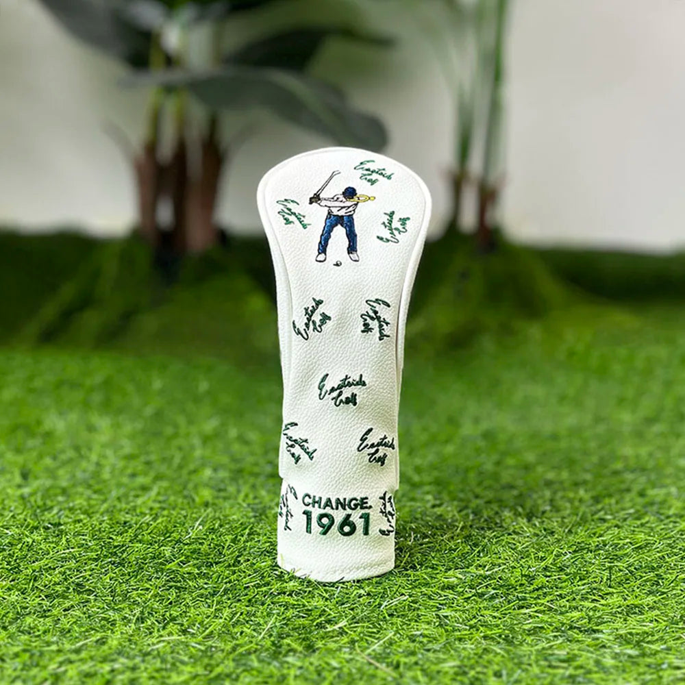 A white golf club head cover featuring a silhouette of a golfer and the text CHANGE 1961, placed on green grass.