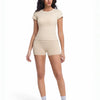 A woman models a beige two-piece workout set consisting of a short-sleeved top and matching shorts.