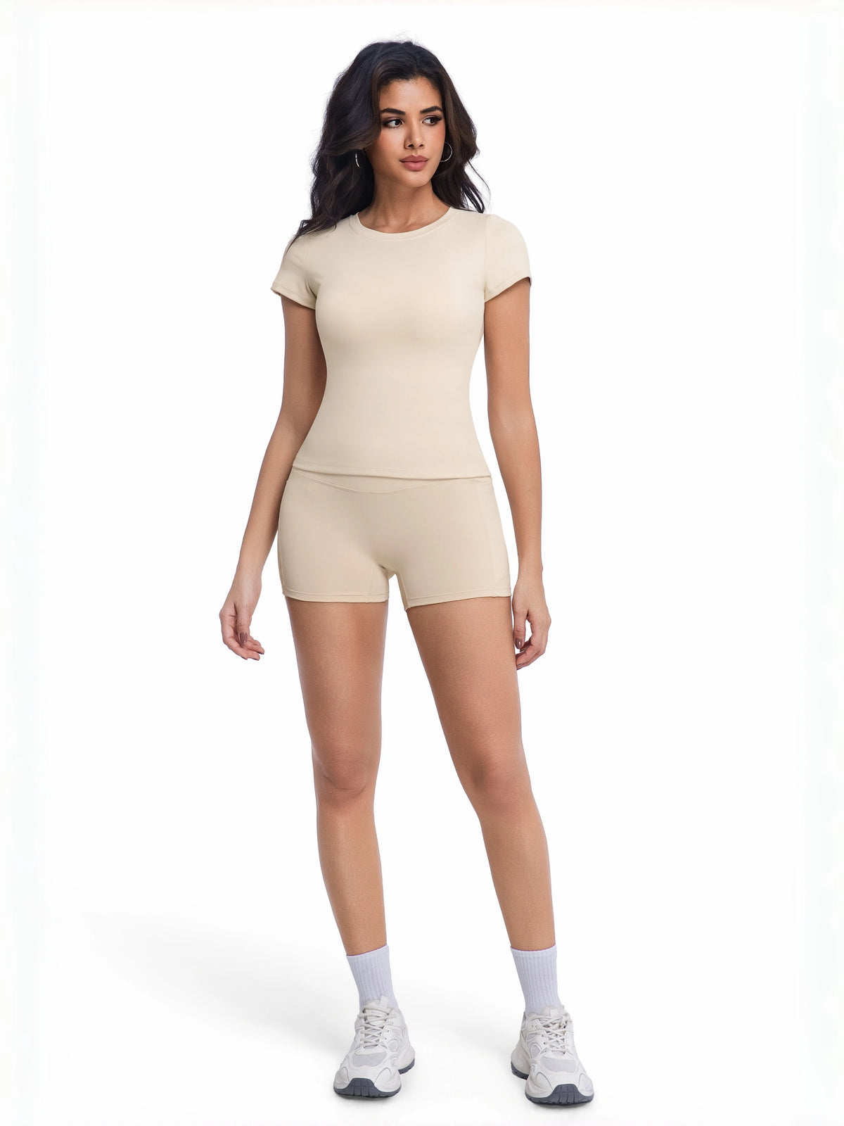 A woman models a beige two-piece workout set consisting of a short-sleeved top and matching shorts.