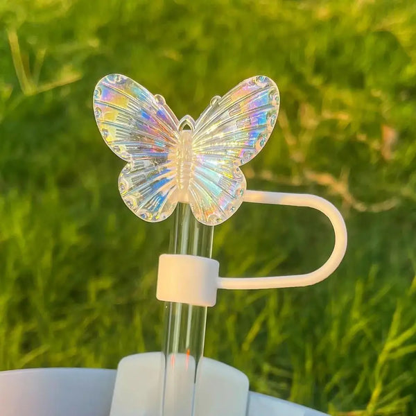 Una cubierta de pajita de mariposa de silicona transparente sobre una pajita de vidrio, con un fondo verde y desenfocado al a