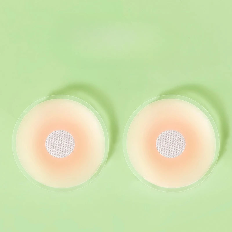 Une paire de cache-laittes en silicone réutilisables, rose pâle, sont présentées sur un fond vert pâle.