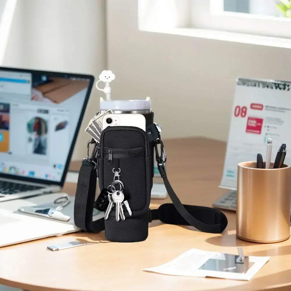 A black neoprene water bottle carrier bag with a shoulder strap resting on a wooden table next to a laptop and papers.