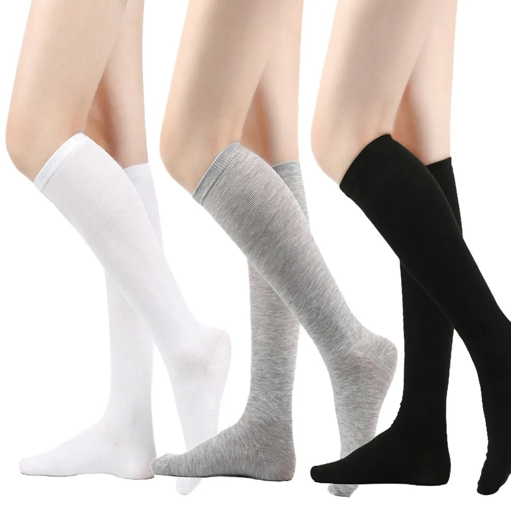 Un conjunto de medias hasta el muslo para mujer en colores blanco, gris y negro mostrados en una pierna.