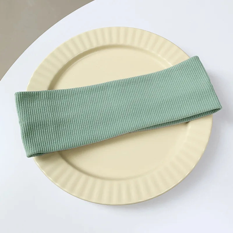 A light sage green elastic hairband is placed on a pale yellow plate.