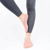 Un par de calcetines antideslizantes rosas puestos en un pie, combinados con leggings grises oscuros.
