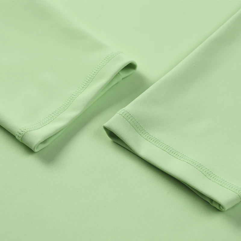 Una camiseta de yoga y running de manga larga, transpirable, color verde claro, doblada sobre una superficie.