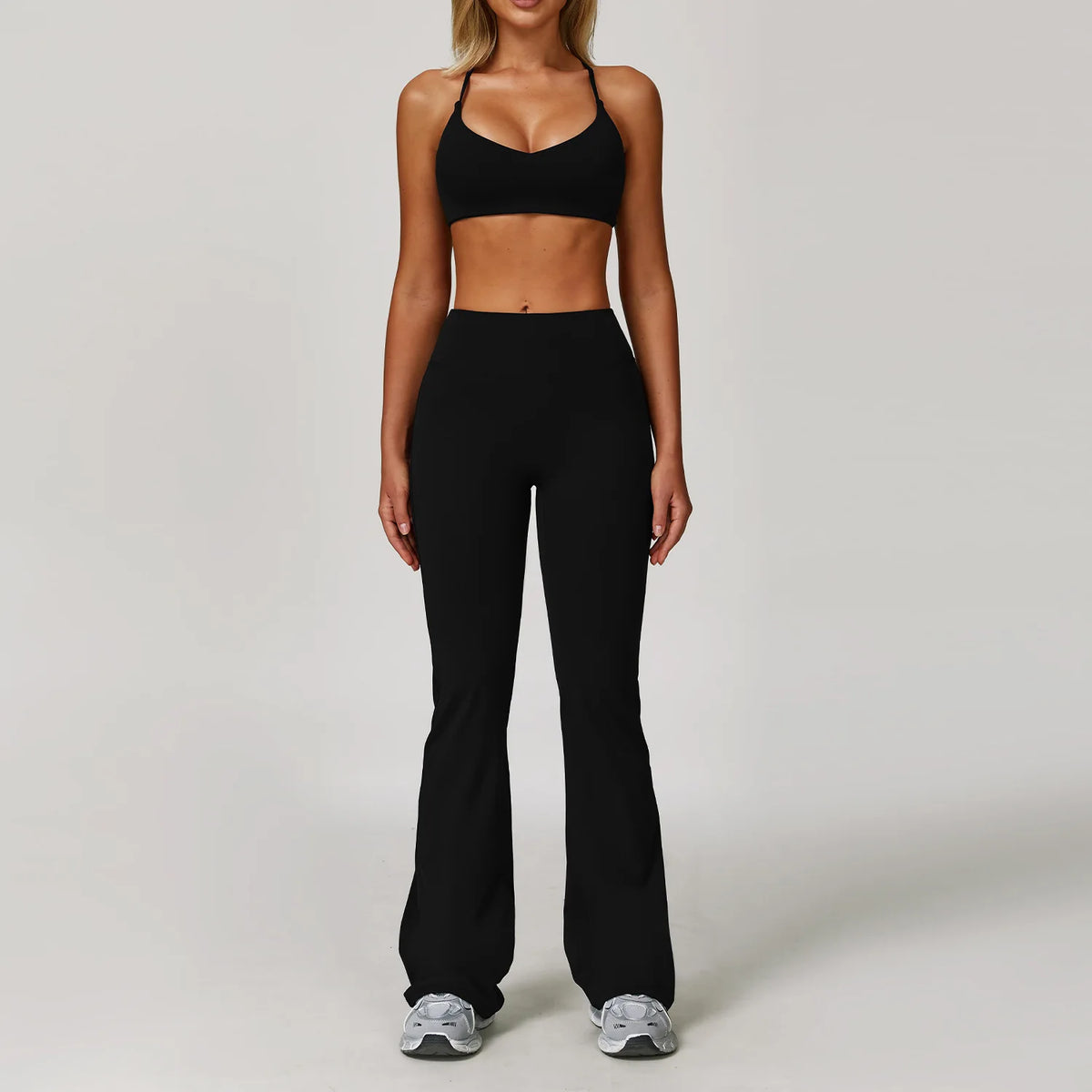 A woman models a black 3-piece yoga sports set consisting of a crop top and high-waisted leggings.
