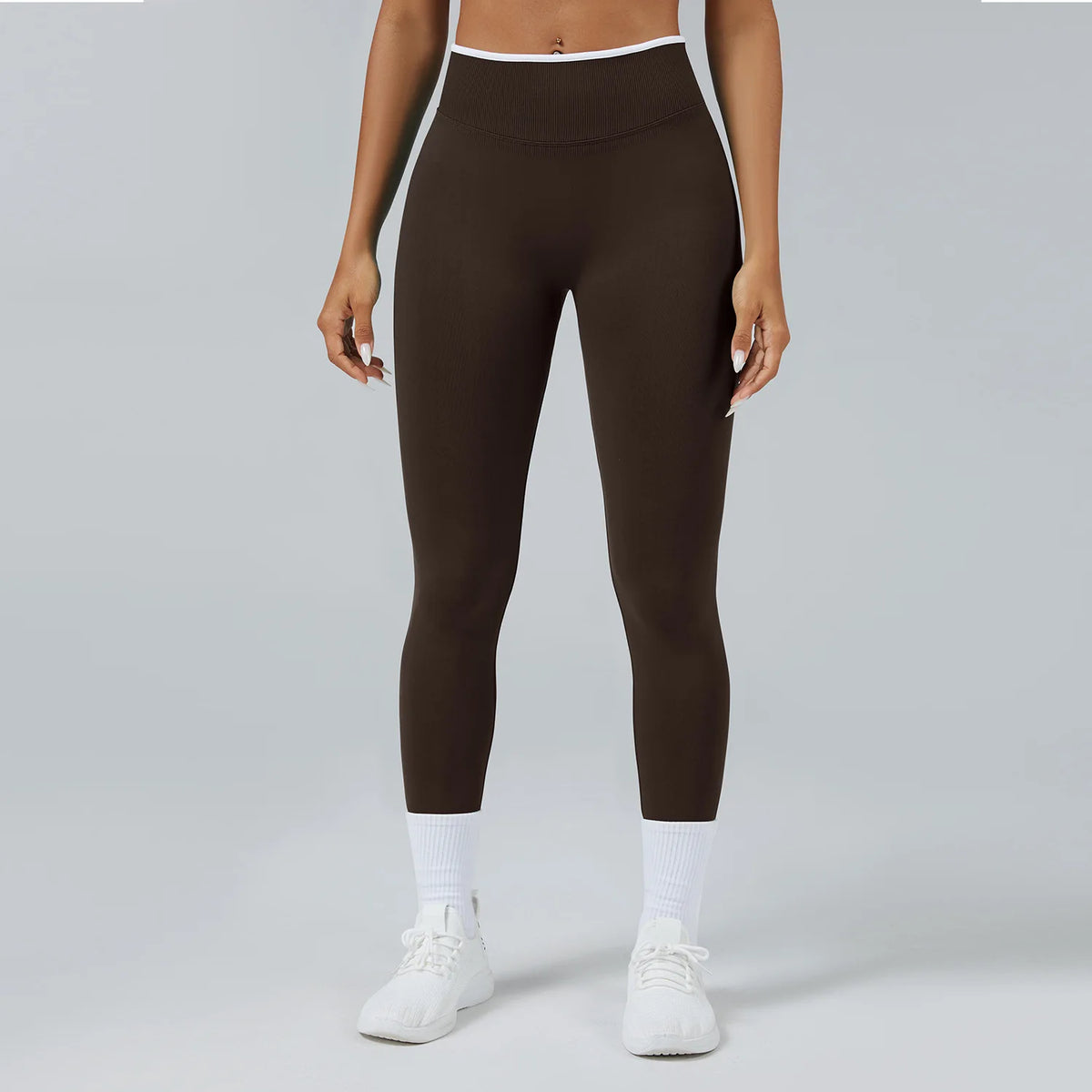 A person wearing dark brown high-waist yoga leggings with white trim and white socks, standing against a light gray backgroun
