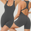 A woman wearing a gray backless fitness jumpsuit, shown from the side.