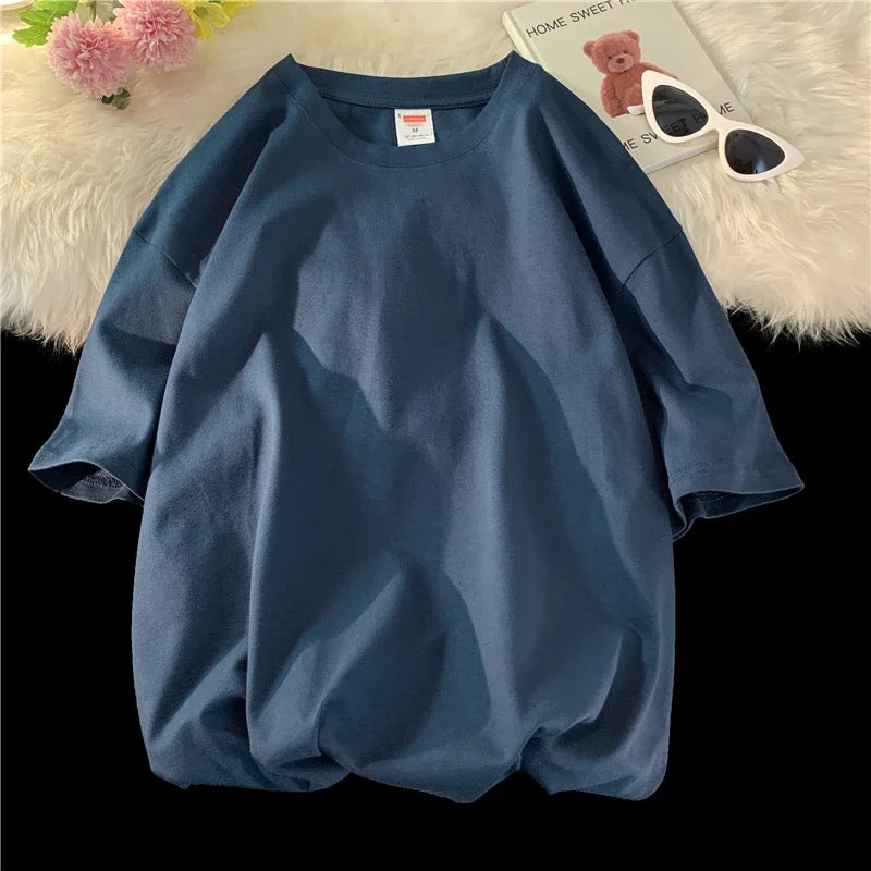 Dunkelblaue, oversized Baumwoll-T-Shirt einer Frau auf einer weißen, flauschigen Oberfläche neben Sonnenbrille.