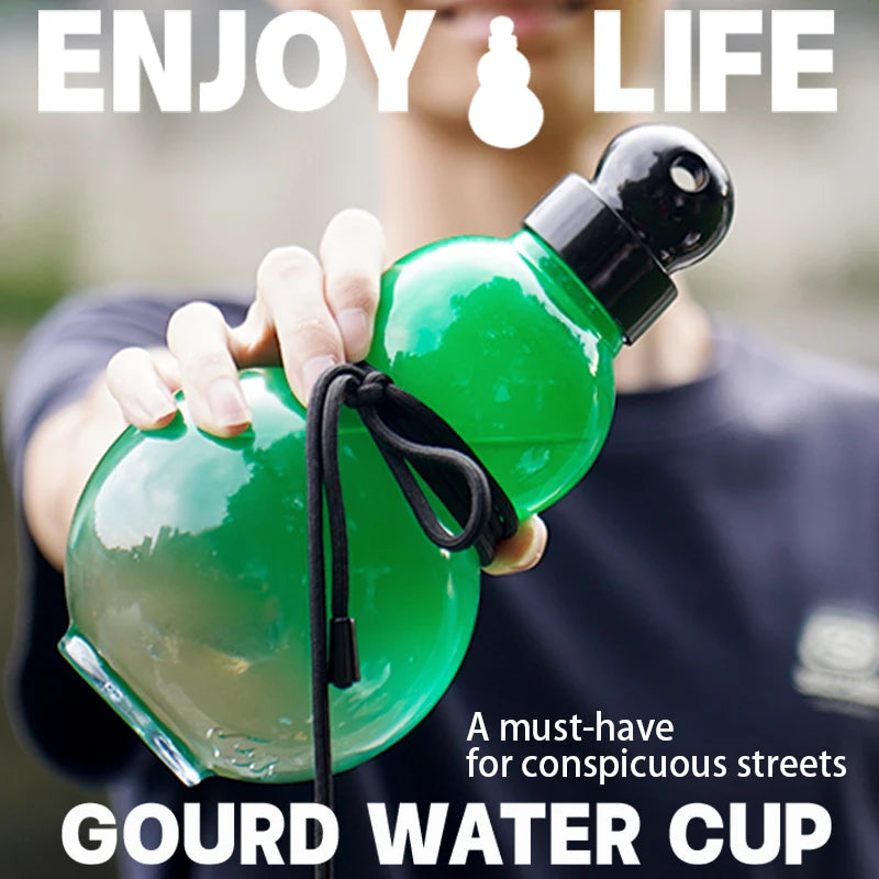 Eine Hand hält eine grüne Kürbis-Wasserflasche mit schwarzem Trageriemen vor einem verschwommenen Hintergrund.