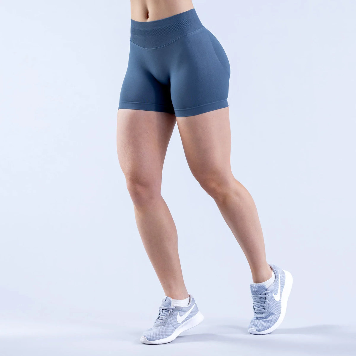A person is wearing navy blue seamless high-waisted yoga shorts and white athletic shoes.