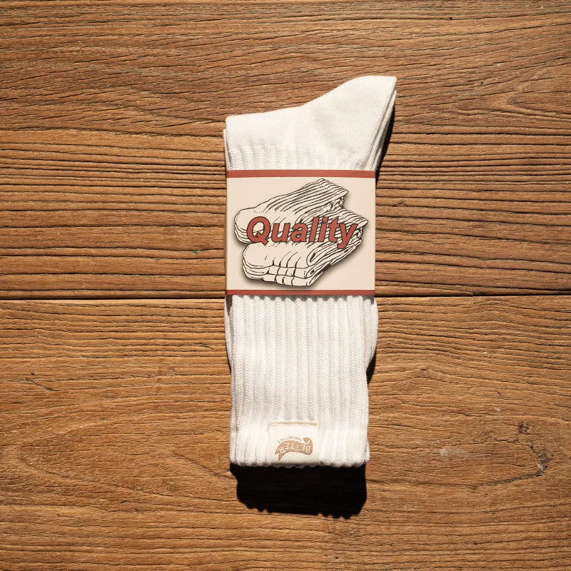 A pair of white tube socks featuring a graphic design with the word Quality on a beige background.