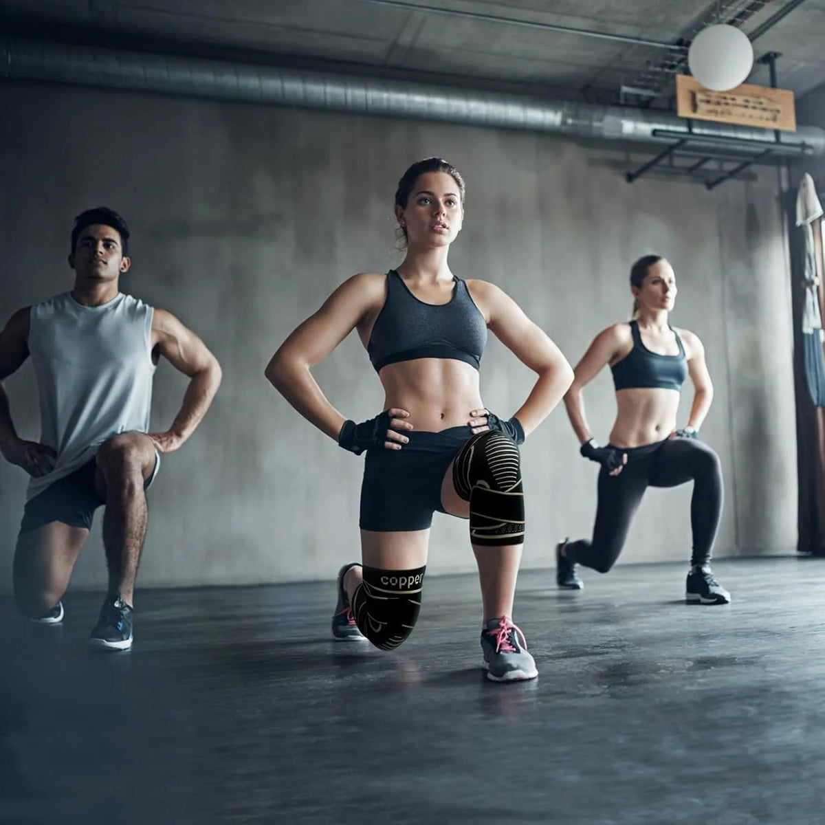 Three individuals exercising in a gym setting, demonstrating the use of copper knee braces.