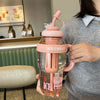 A person holds a large capacity portable plastic drinking cup with a pink lid and orange liquid.