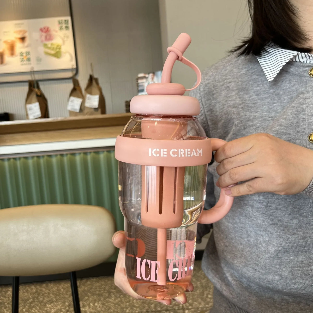 A person holds a large capacity portable plastic drinking cup with a pink lid and orange liquid.