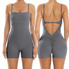A woman models a gray backless fitness jumpsuit from the rear view.