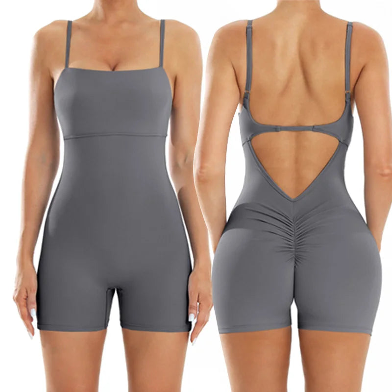 A woman models a gray backless fitness jumpsuit from the rear view.