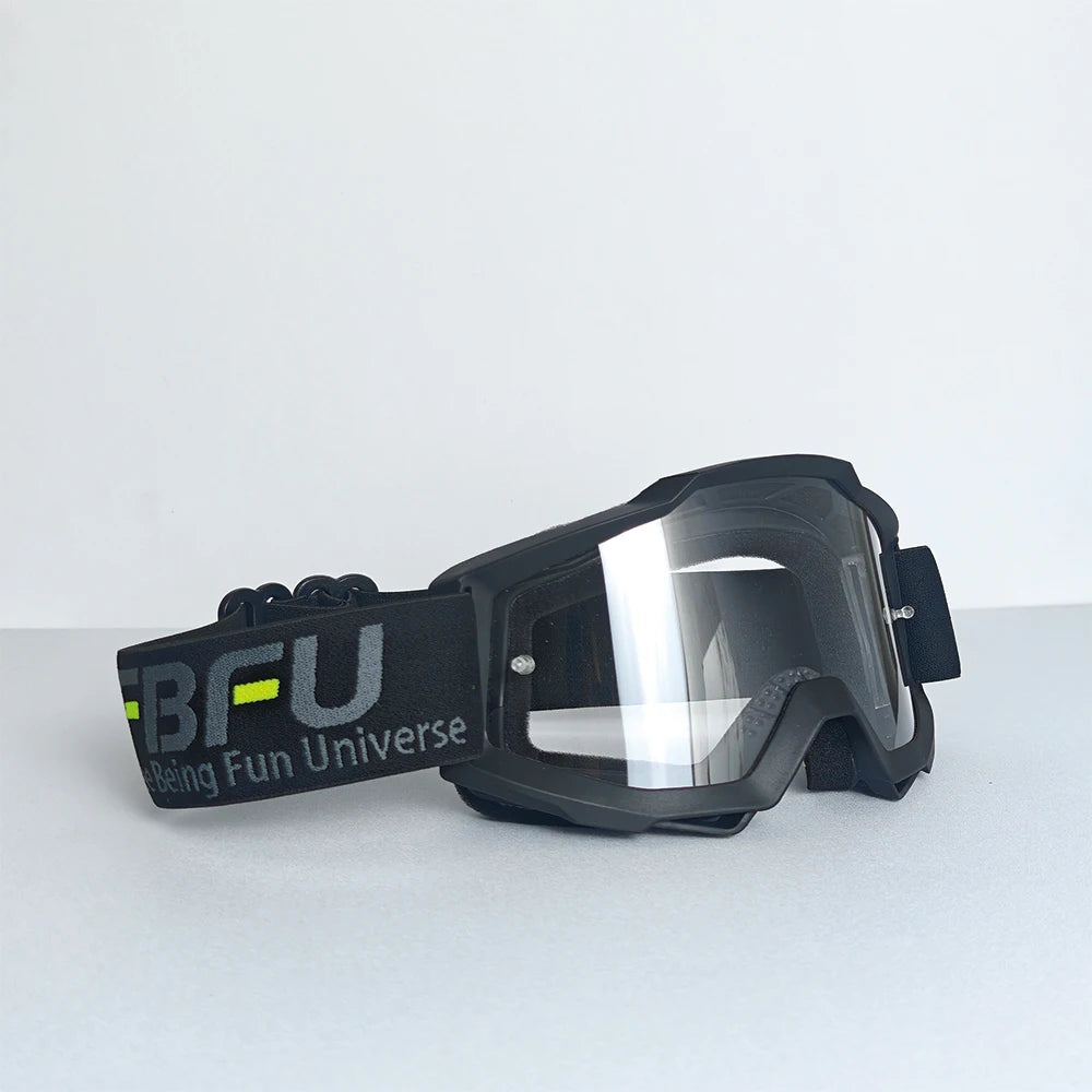 Black sport-grade skiing goggles with a black strap and clear lenses resting on a light surface.
